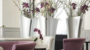 A modern interior with white vases containing purple orchids, a white sofa, and two pink chairs. - Hôtel Esplanade Eden (Lourdes)