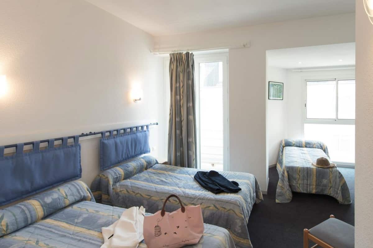 A hotel room with two beds, a window with curtains, a chair, and a small table.