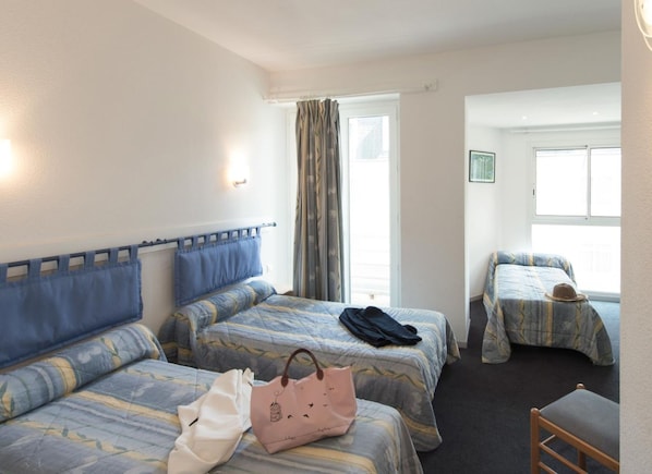 A hotel room with two beds, a window with curtains, a chair, and a small table. - Hôtel Esplanade Eden (Lourdes)