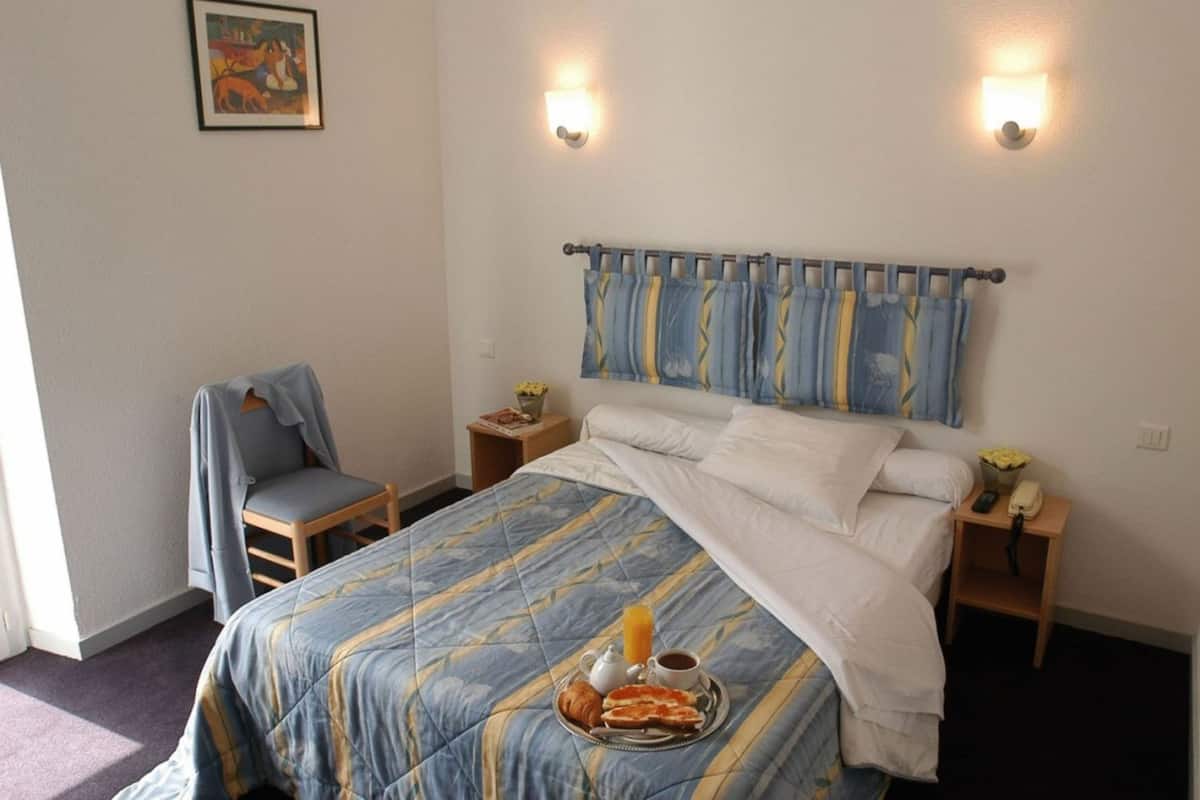 A hotel room with a bed, a chair, a bedside table with a lamp, and a painting on the wall.