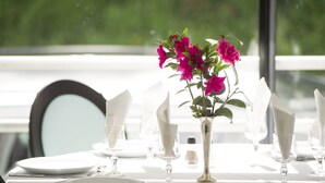 A table set for dining with white tablecloths, plates, and silverware, and a vase with pink flowers. - Hôtel Esplanade Eden (Lourdes)