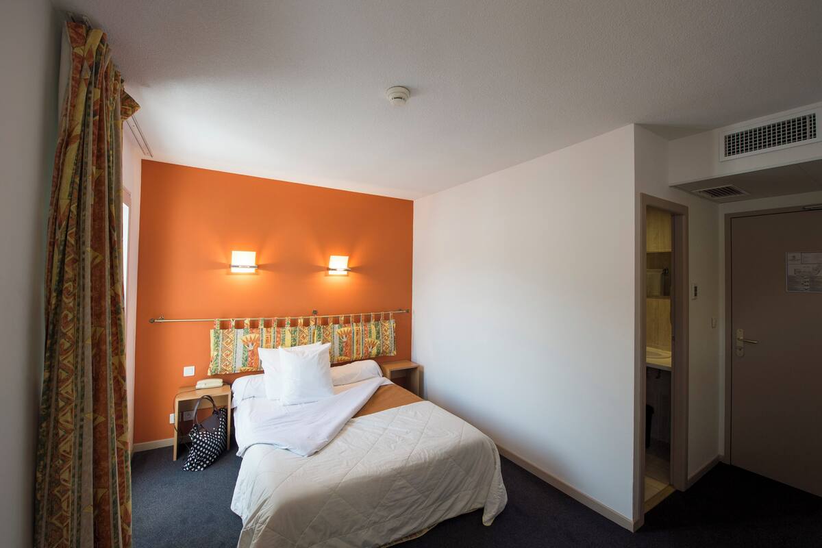 A hotel room with a bed, a nightstand, a lamp, and a wardrobe.