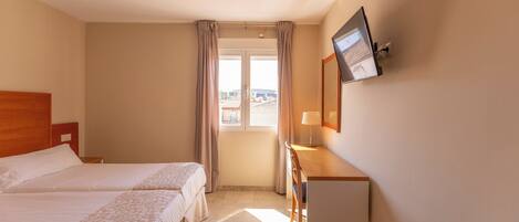 A hotel room with two beds, a desk, a television, and a window with curtains.