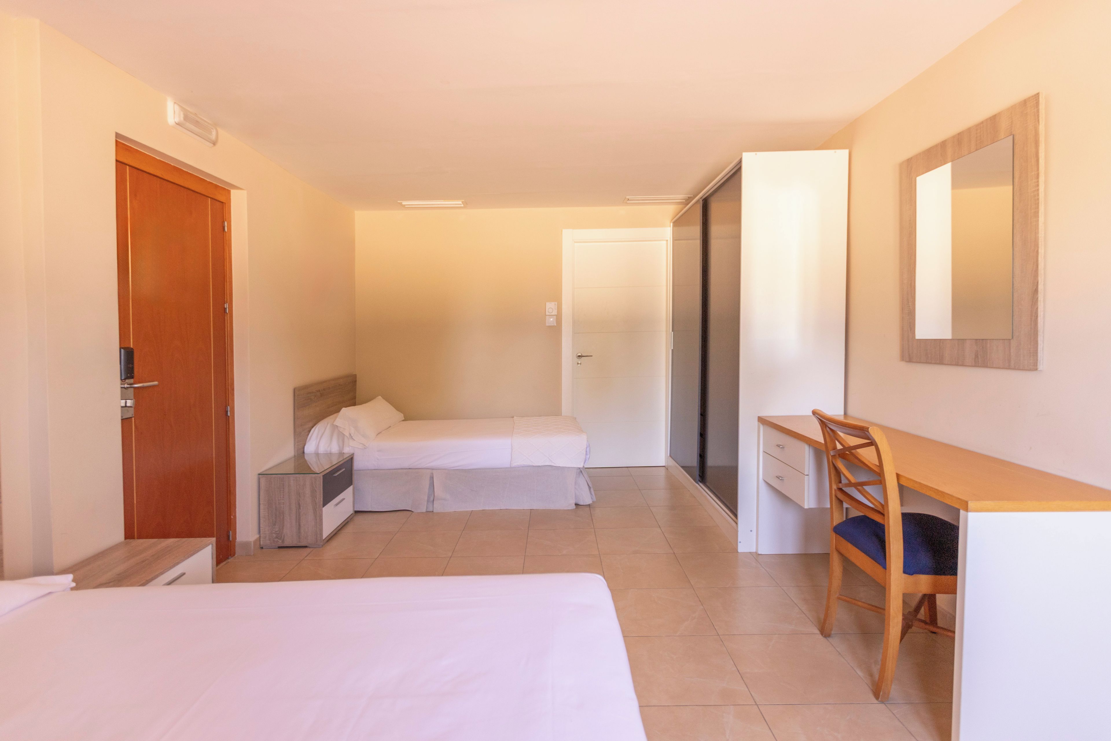 Una habitación de hotel con dos camas, un escritorio, una silla, un armario y un espejo.