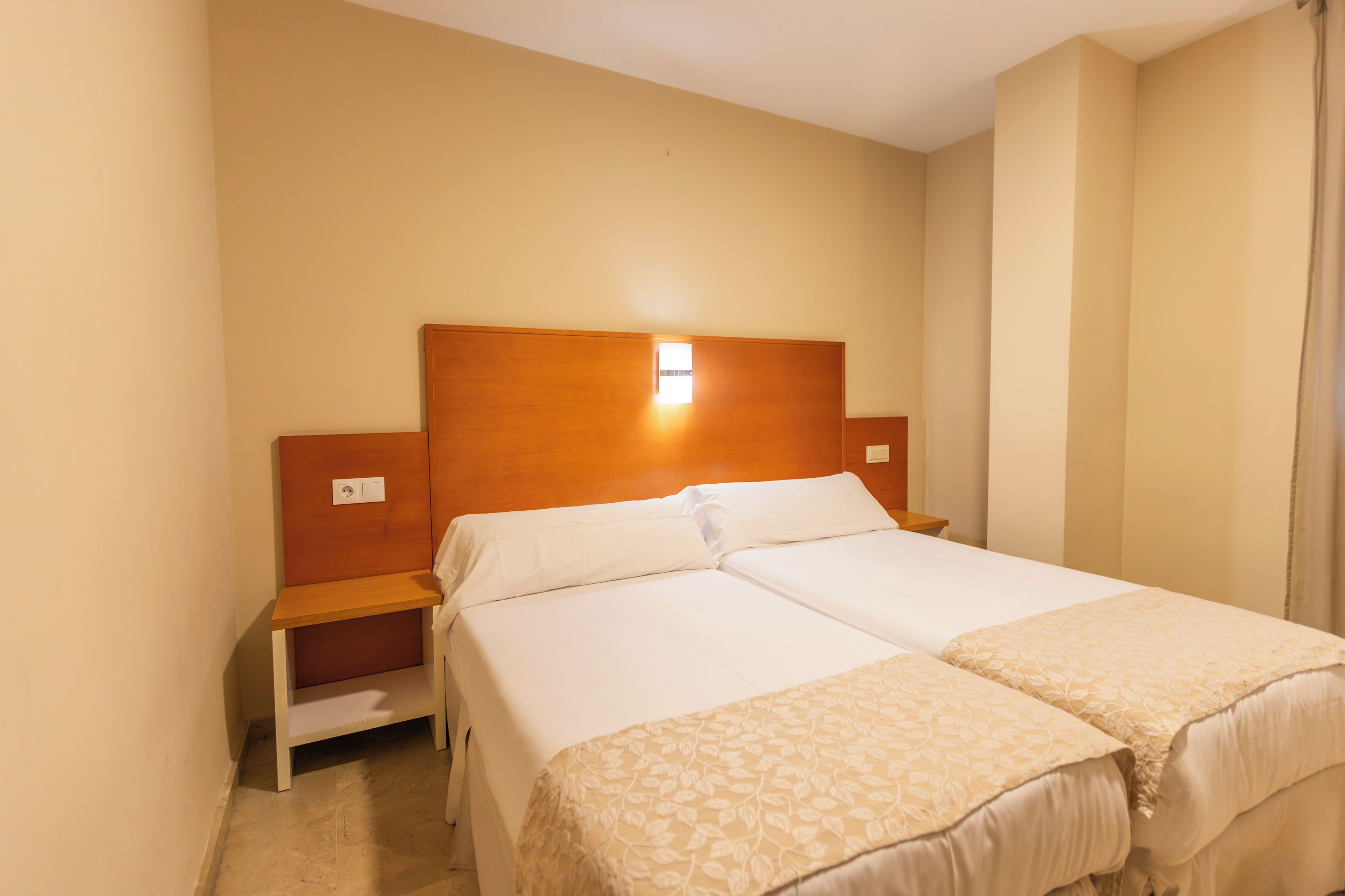 A double bed with a wooden headboard, a nightstand, and a bedside table in a hotel room.