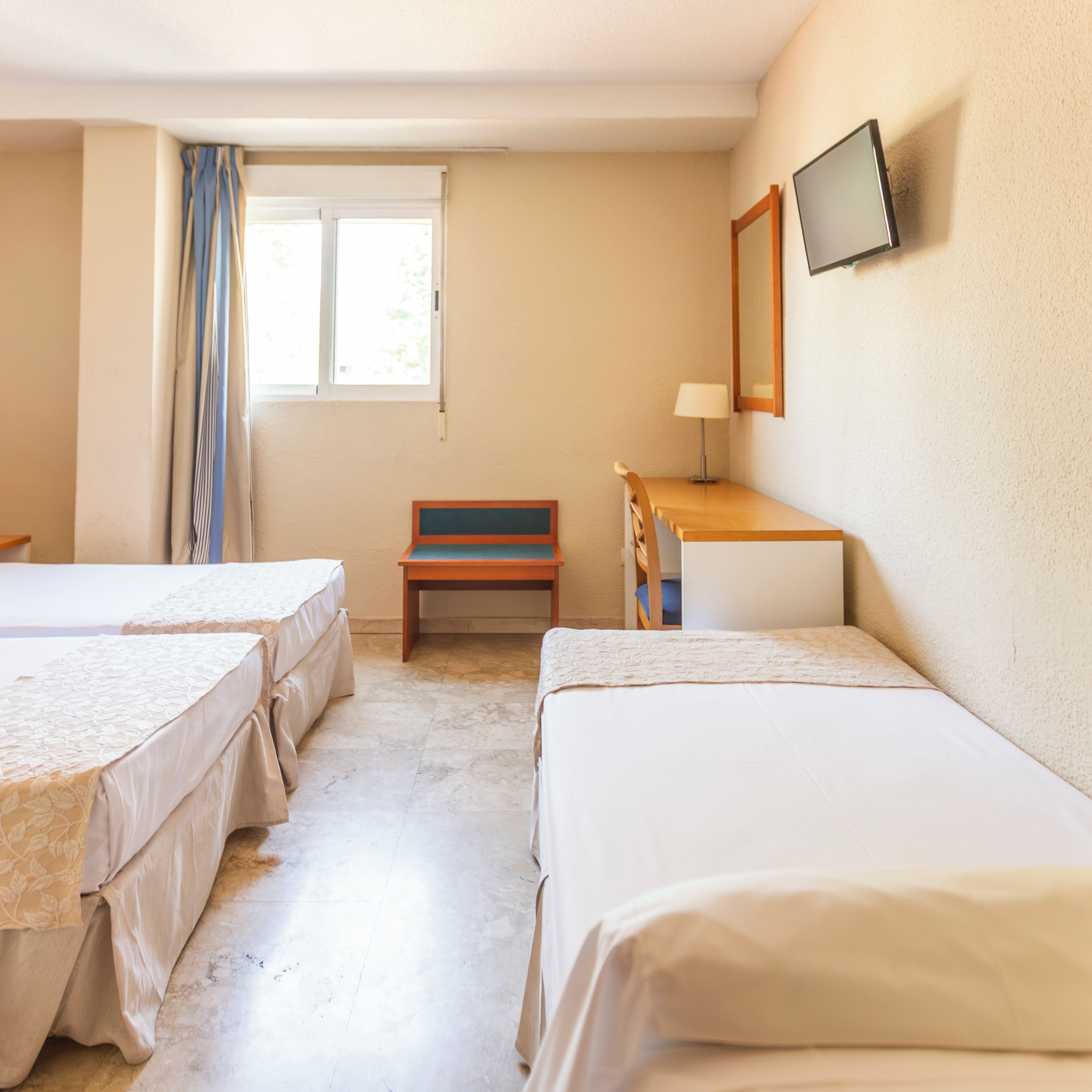 A hotel room with two beds, a desk, a chair, a window with curtains, and a television on the wall.