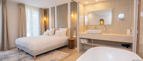 A modern bedroom with a large bed, a separate bathroom with a bathtub, and a vanity with a mirror.