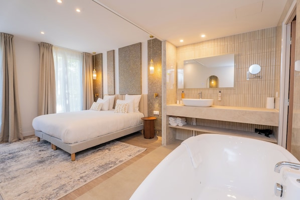 A modern bedroom with a large bed, a separate bathroom with a bathtub, and a vanity with a mirror.
