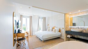 A modern hotel room with a large bed, a separate bathroom with a large bathtub, a desk with a chair, and a large mirror. - BOBO'S HÔTEL  (Paris)