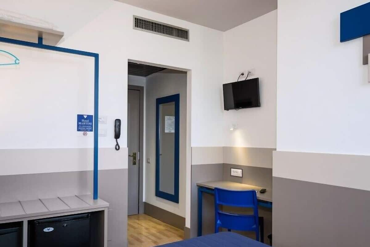 Habitación de hotel con cama, escritorio, silla, televisor, teléfono y minibar.