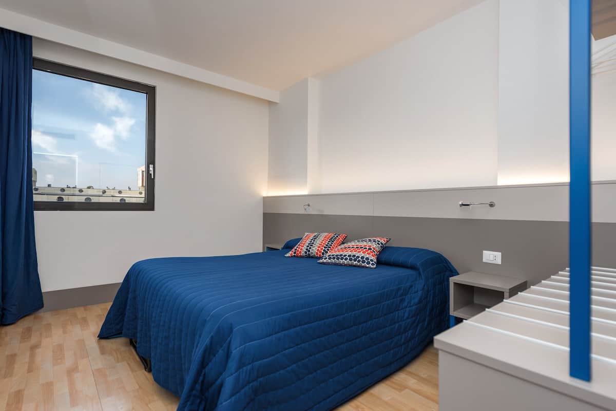 Un dormitorio moderno con una cama grande, una mesita de noche, un aparador y un ventanal con cortinas.
