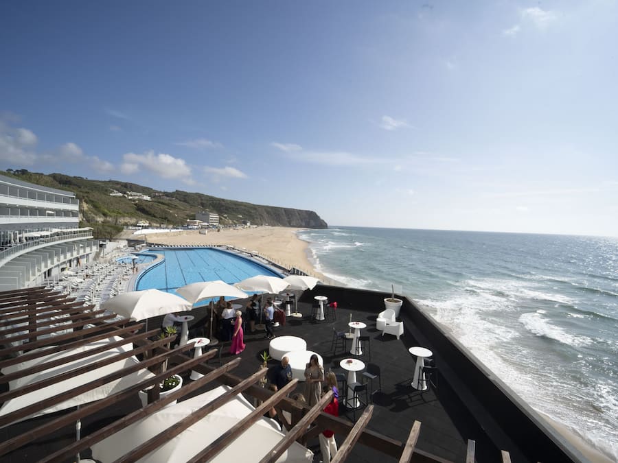 A deck with outdoor seating overlooking a beach and a pool.