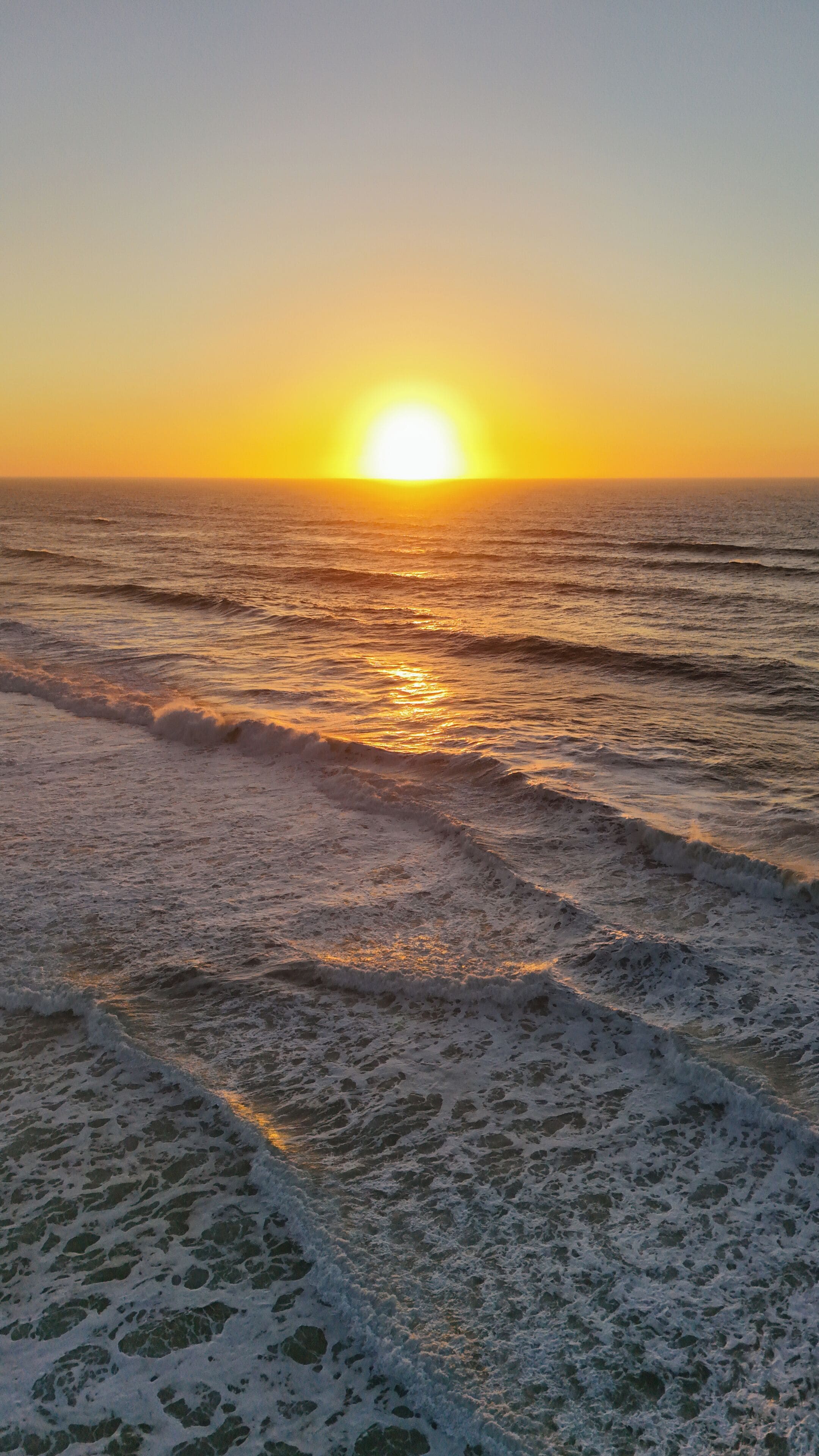 A sunset over the ocean with waves approaching the shore.