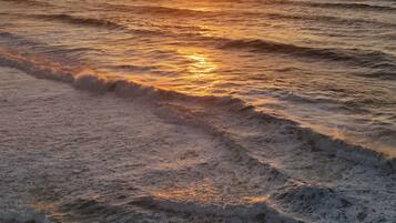 A sunset over the ocean with waves approaching the shore.