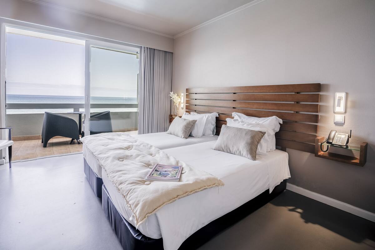 Een hotelkamer met een groot bed, een klein tafeltje, een stoel en een balkon met uitzicht op zee.