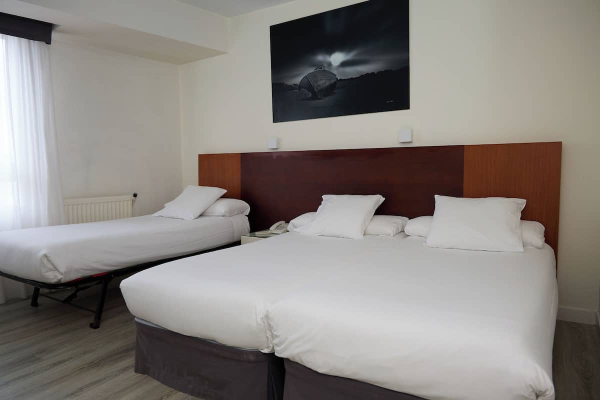 A hotel room with two single beds, a wooden headboard, a nightstand with a phone, and a large black and white artwork on the wall.