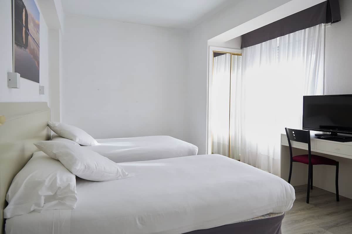 A hotel room with two beds, a desk with a chair, and a television.