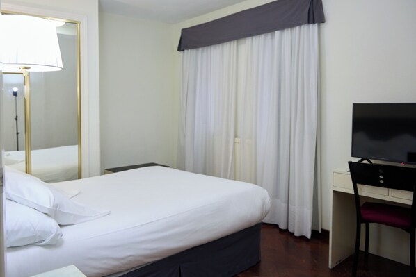 A hotel room with a bed, a desk, a chair, a television, and a window with curtains. - Hotel Vigo Plaza (Vigo)