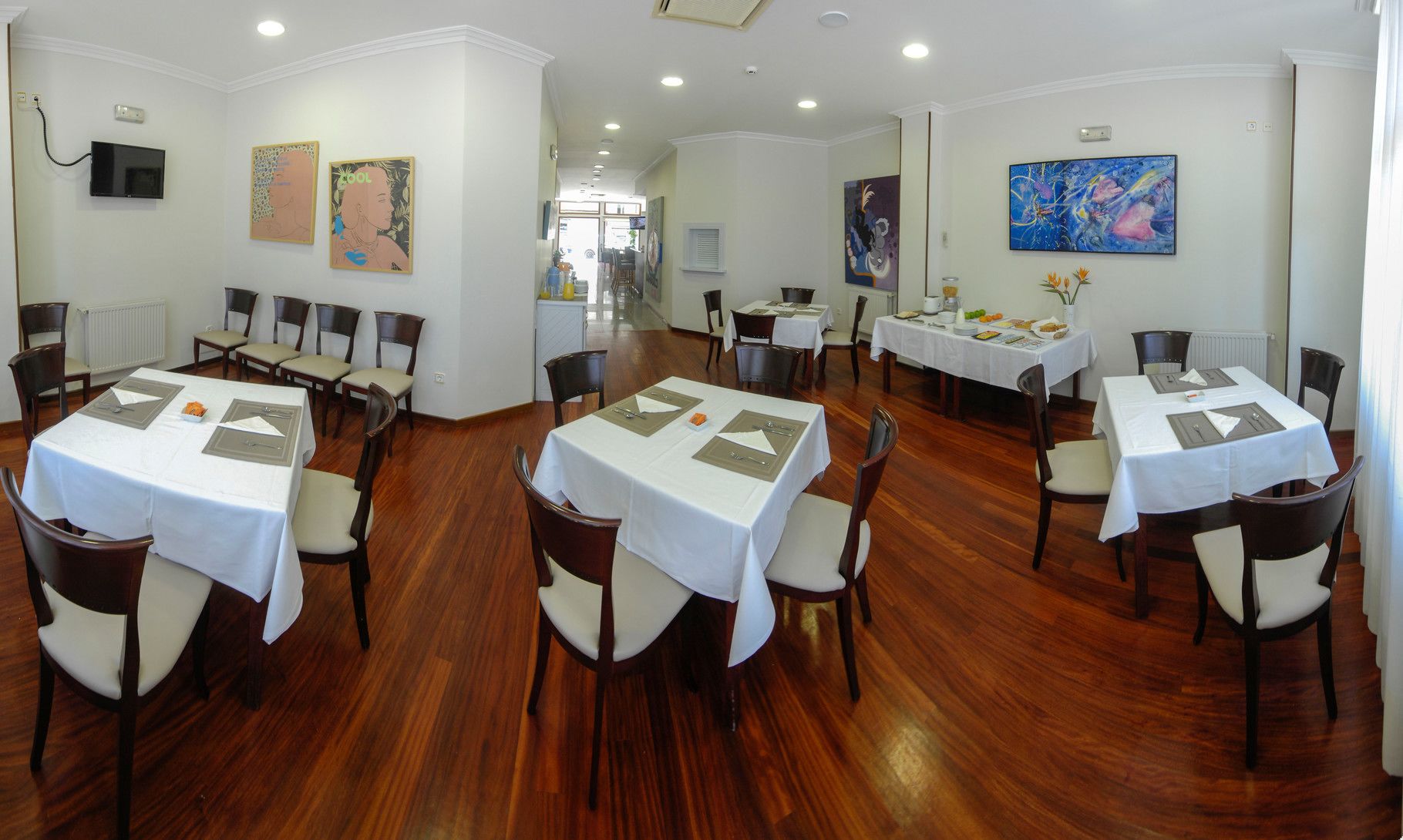 A dining area with multiple tables set for meals, chairs, and artwork on the walls.