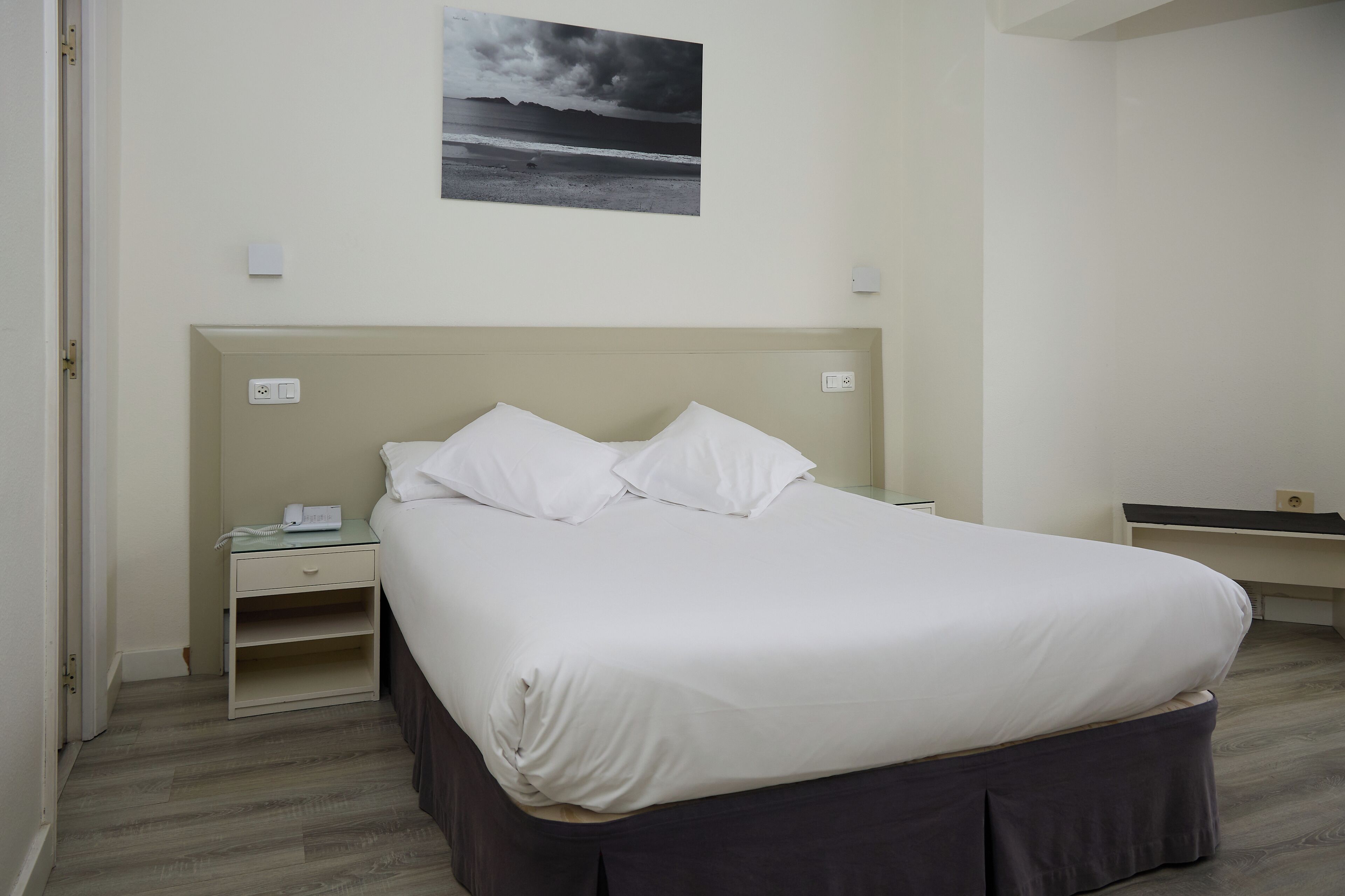 A neatly arranged bedroom with a bed, bedside table, and a wall-mounted picture.
