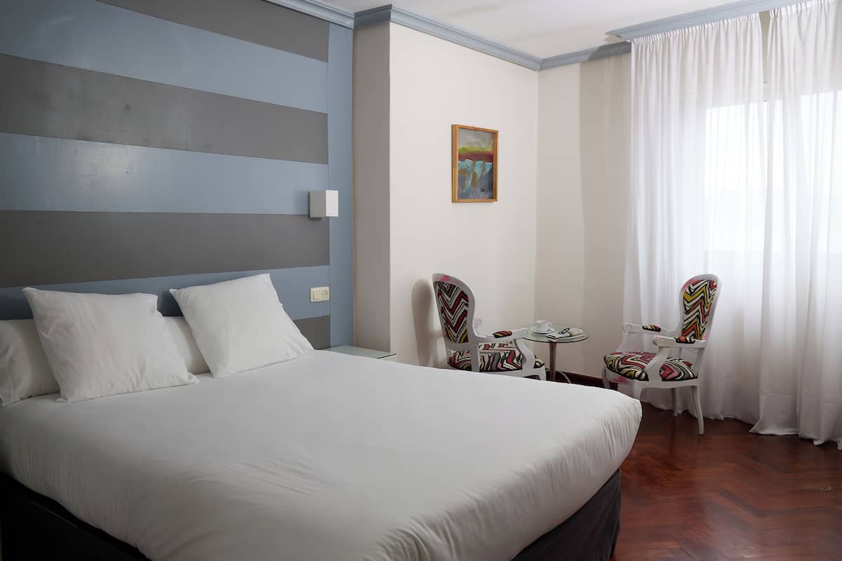 A hotel room with a large bed, two chairs, a small table, and a painting on the wall.