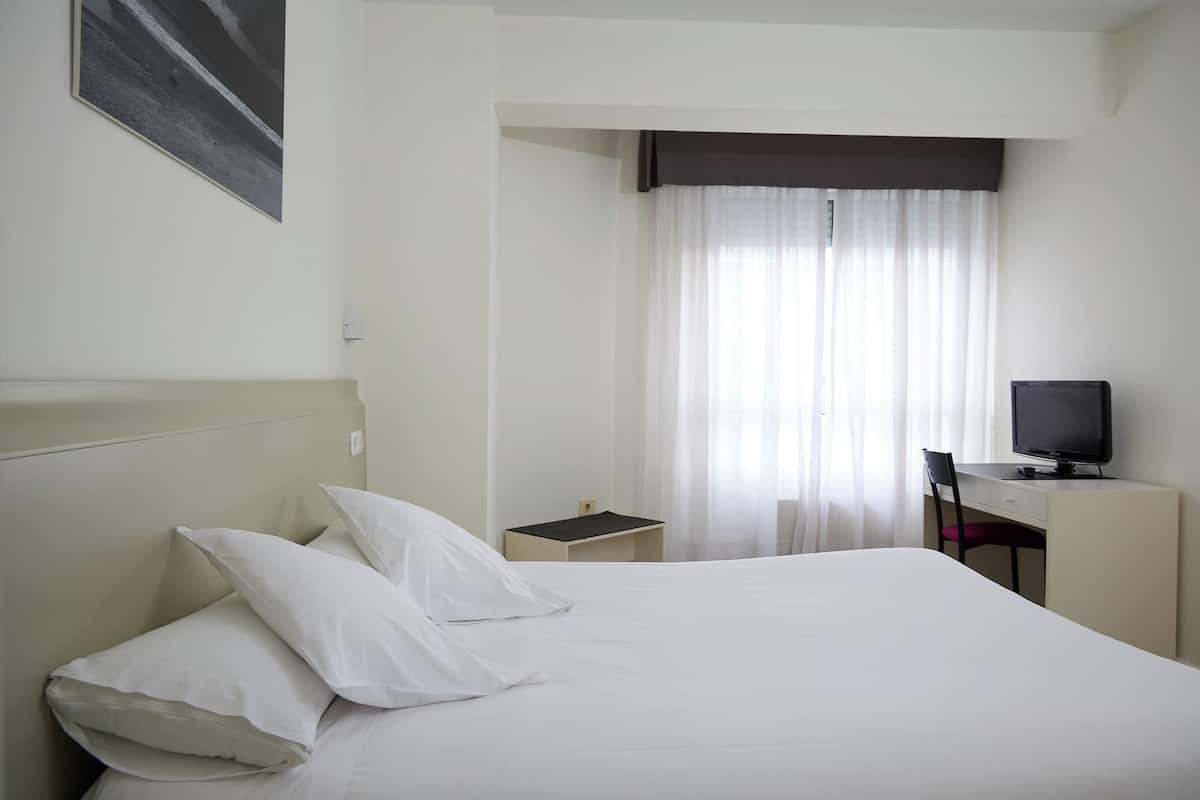 A hotel room with a bed, a desk, a chair, a television, and a window with curtains.