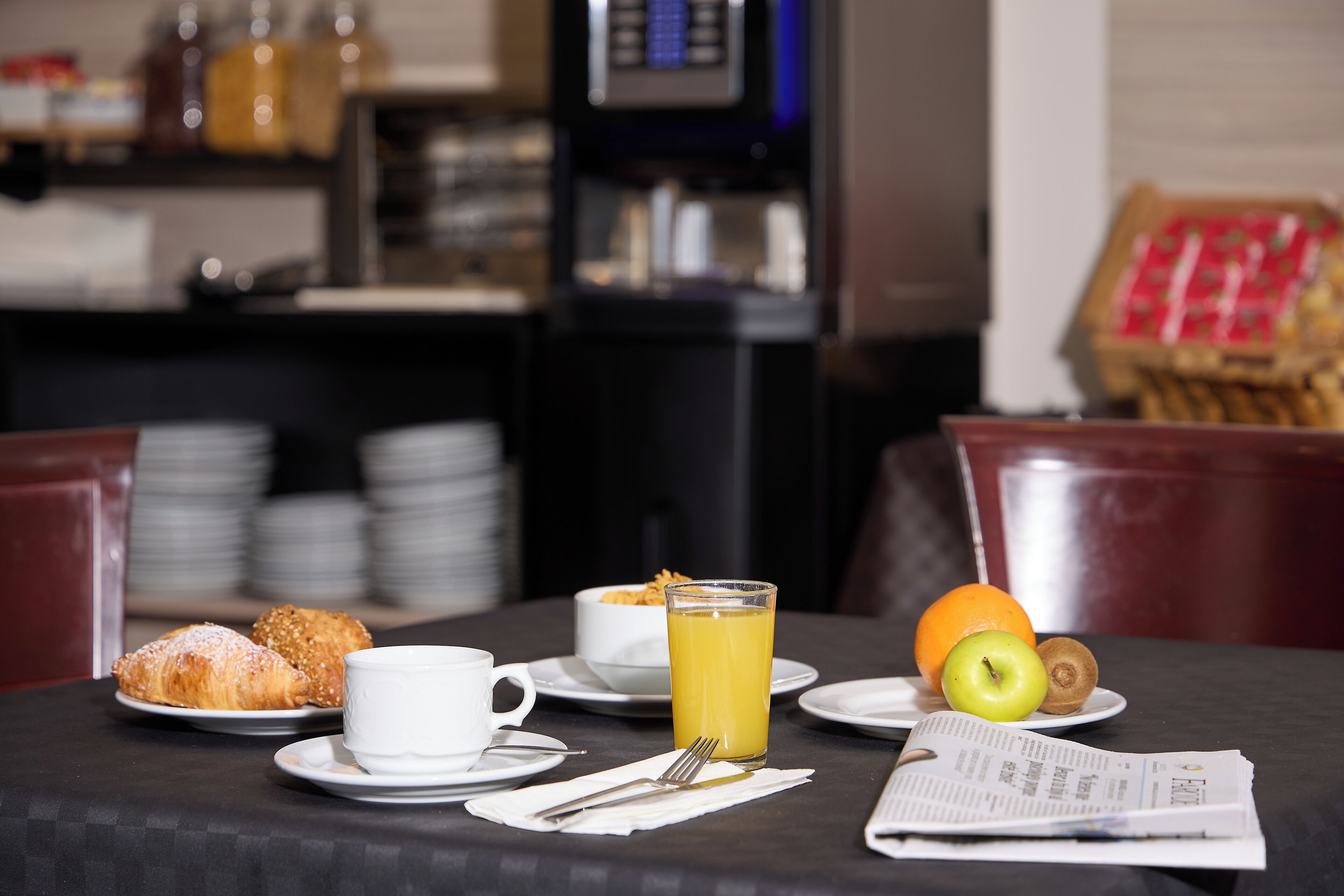 Un desayuno con cruasanes, jugo de naranja, una manzana y un kiwi sobre una mesa.