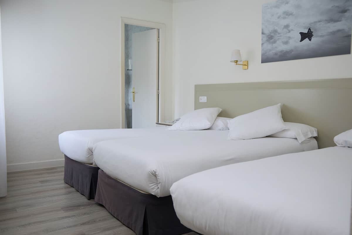 A hotel room with two beds, a door, a wall-mounted light, and a painting of a bird.