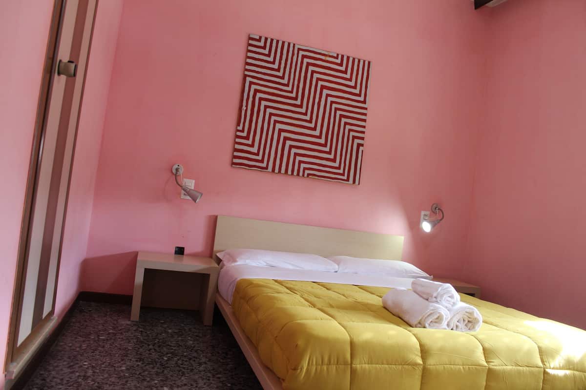 Une chambre d’hôtel avec un lit, une table de chevet, une lampe fixée au mur et un tableau.