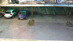 Un área de estacionamiento techada con dos coches aparcados bajo una lona verde.