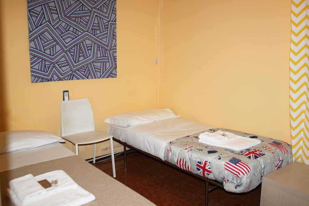 Un lit simple avec une couvre-lit aux motifs de drapeaux, une chaise blanche et une décoration murale à motifs dans une pièce aux murs jaunes.