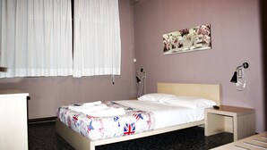 Una cama bien hecha con una colcha estampada, una lámpara de noche, una mesita de noche pequeña y un teléfono instalado en la pared.