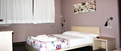Una cama bien hecha con una colcha estampada, una lámpara de noche, una mesita de noche pequeña y un teléfono instalado en la pared.