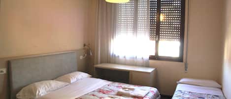Una habitación de hotel con una cama individual, un escritorio pequeño y una ventana con persianas.