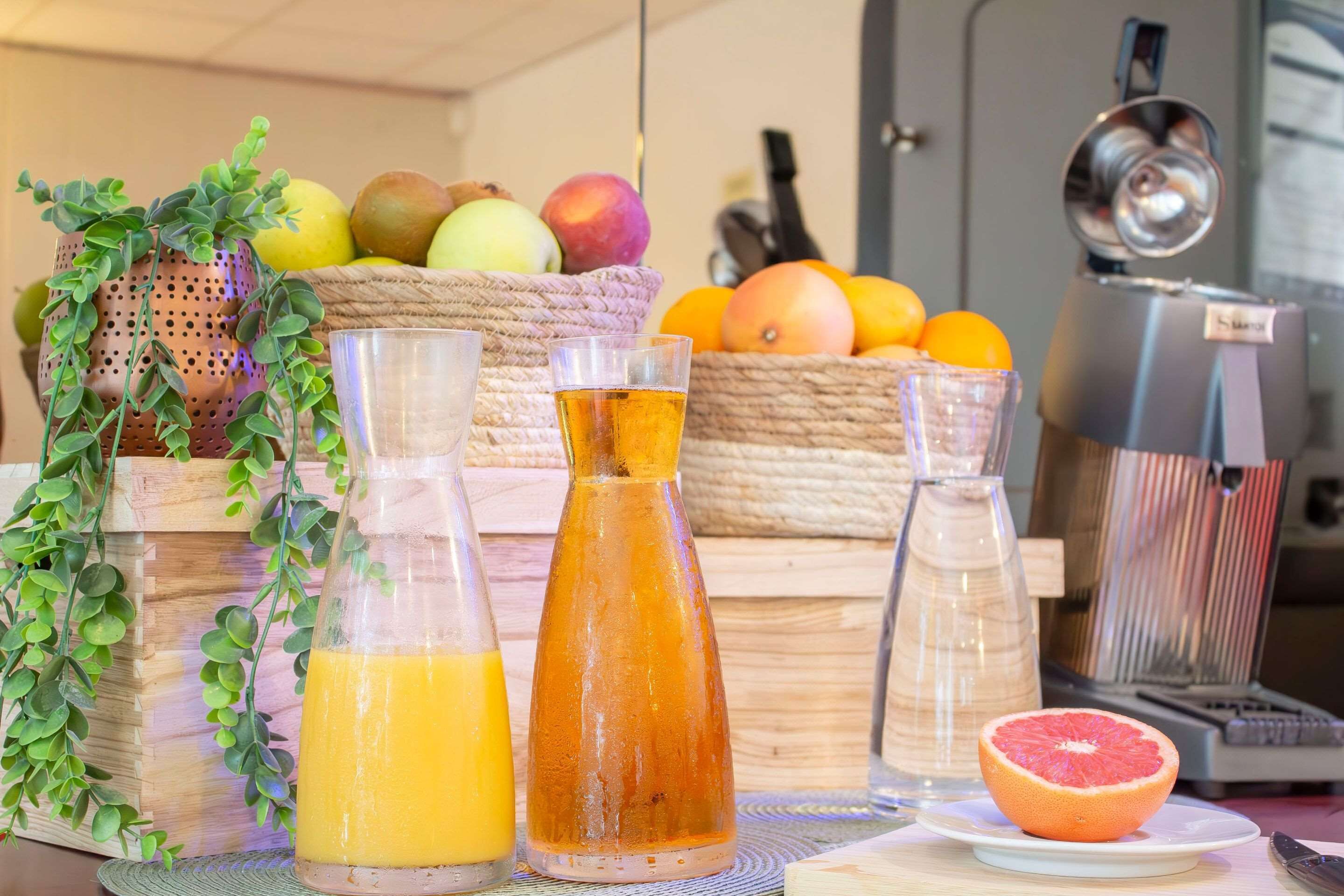 A kitchen counter with a fruit basket, a juicer, and two glass bottles of juice.