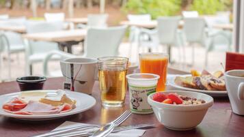 A breakfast table with plates of food, a glass of juice, a cup of coffee, and a bowl of yogurt.