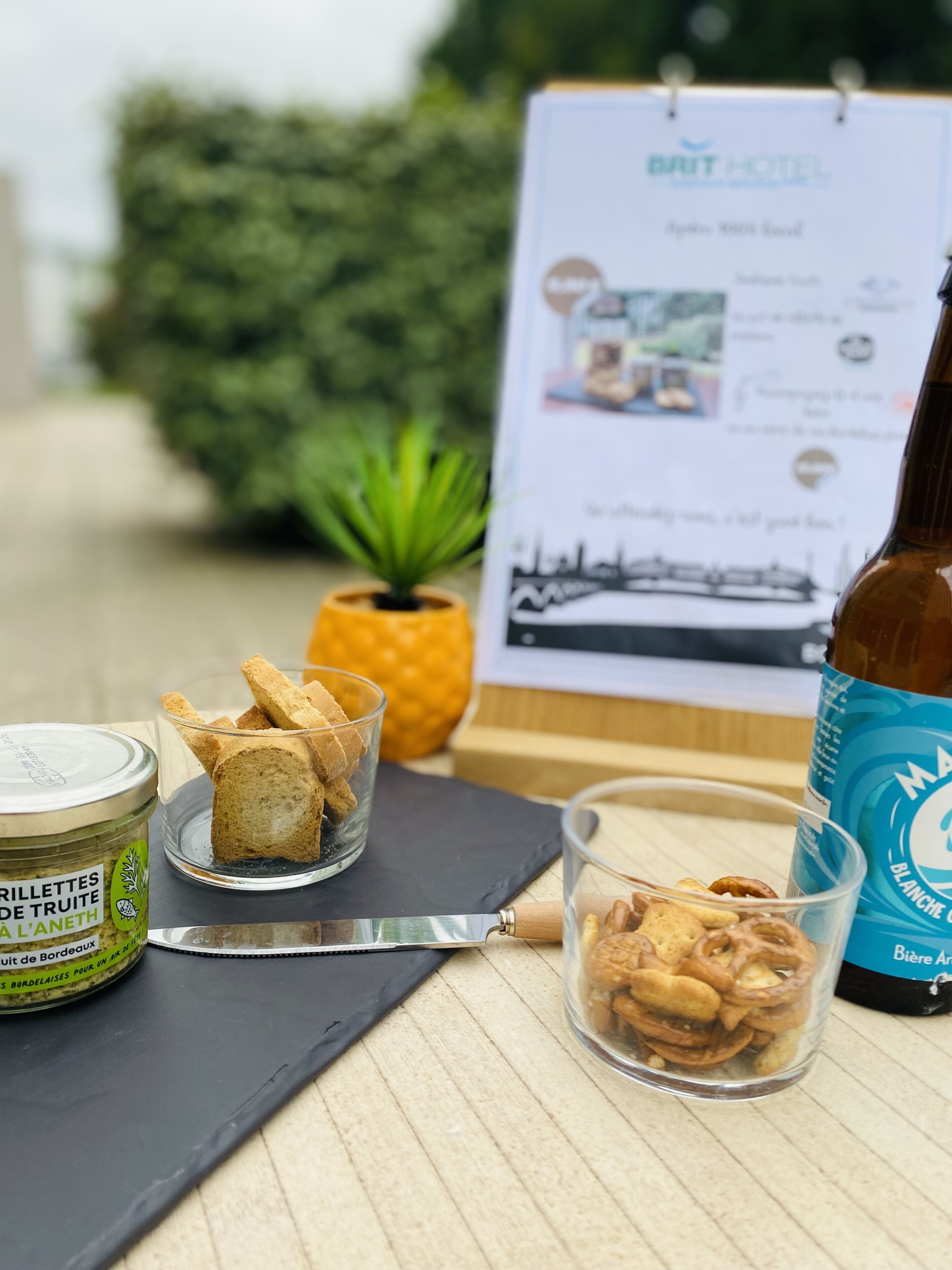 Une table avec une bouteille de bière, un pot de moutarde et deux verres contenant des amuse-gueules.
