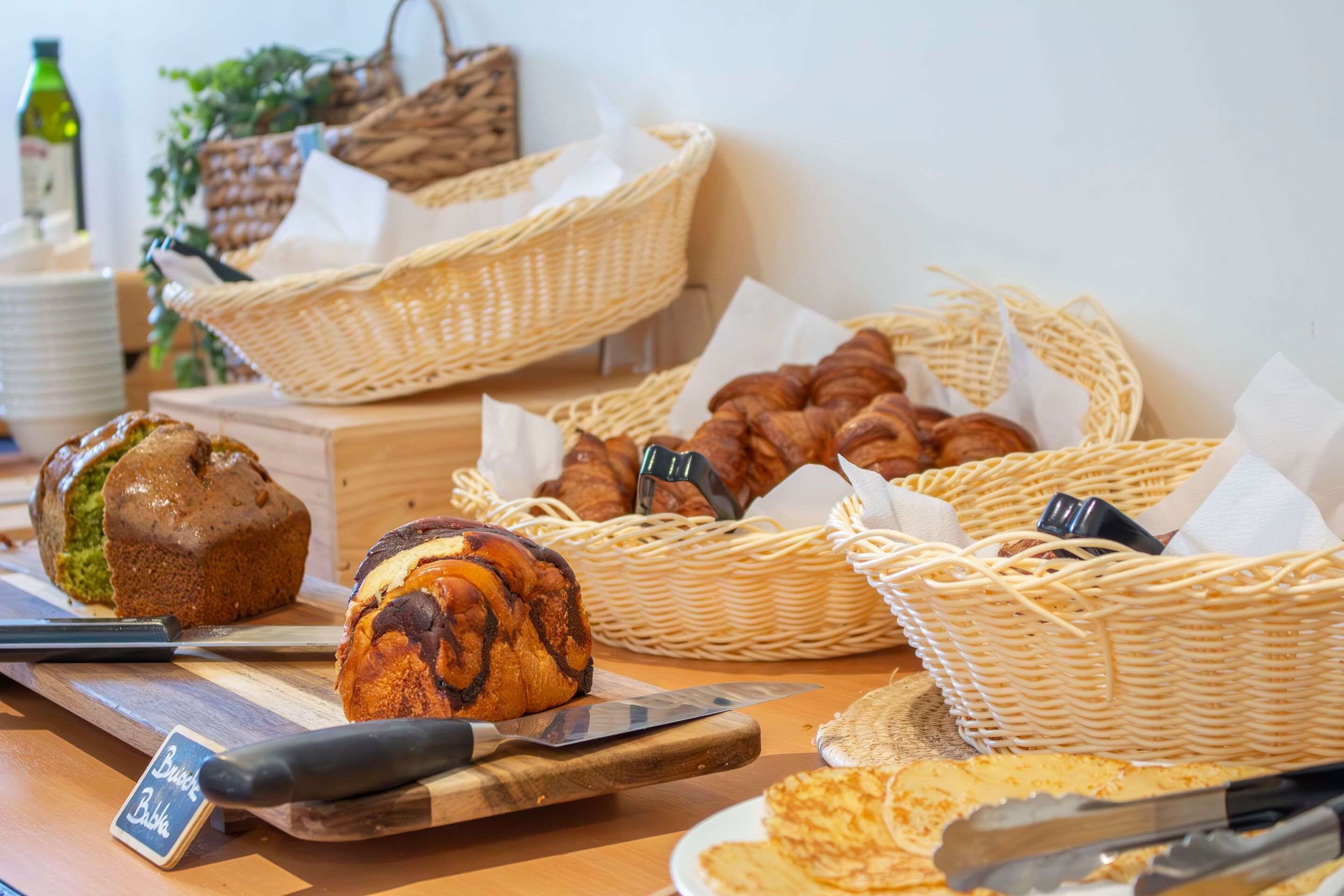 Une variété de produits de boulangerie sont exposés sur une table en bois, notamment du pain et des muffins, avec des paniers et un panneau indiquant l’emplacement du rayon boulangerie.