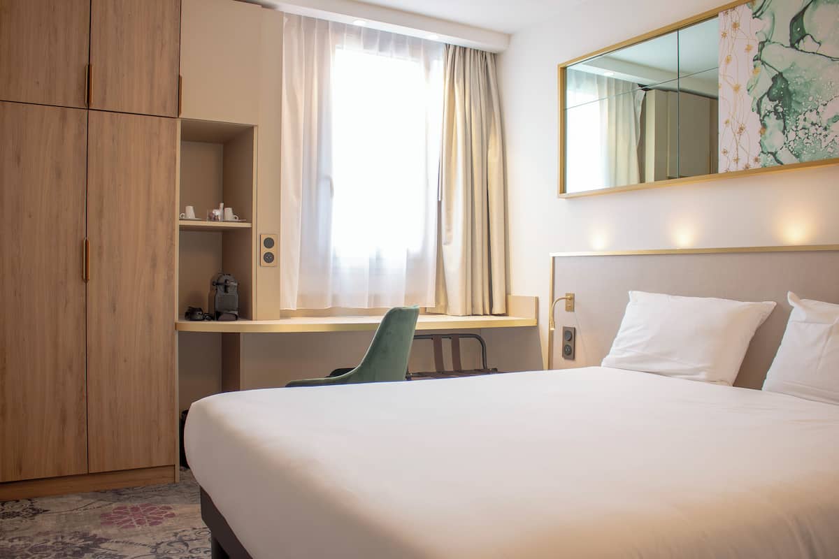 Une chambre d’hôtel avec un lit, un bureau, une chaise et une armoire.