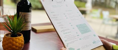 A menu on a wooden table with a bottle of wine and a small plant.