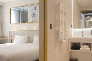 A hotel room with a bed, a large mirror, a white bathroom with a sink and towel rack. - Brit Hotel Bordeaux Aéroport - Le Soretel (Merignac)