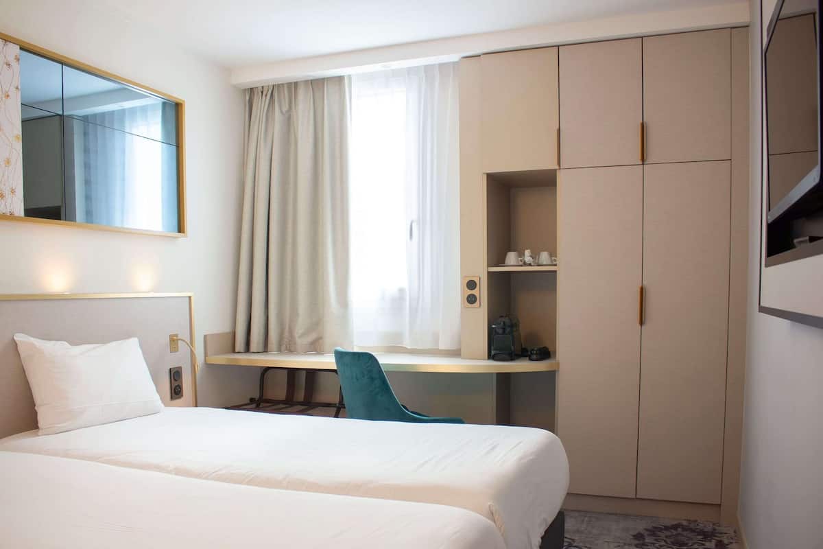 Une chambre d’hôtel comprenant un lit, un bureau, une chaise, une armoire et un grand miroir.