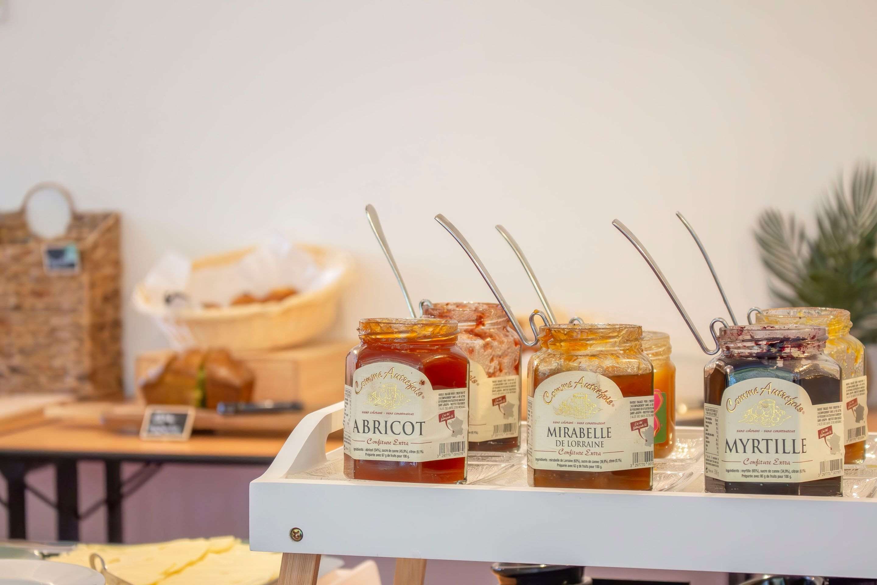 A display of honey jars labeled 'Abricot,' 'Mirabelle de Lorrain,' and 'Myrtille' on a white tray.