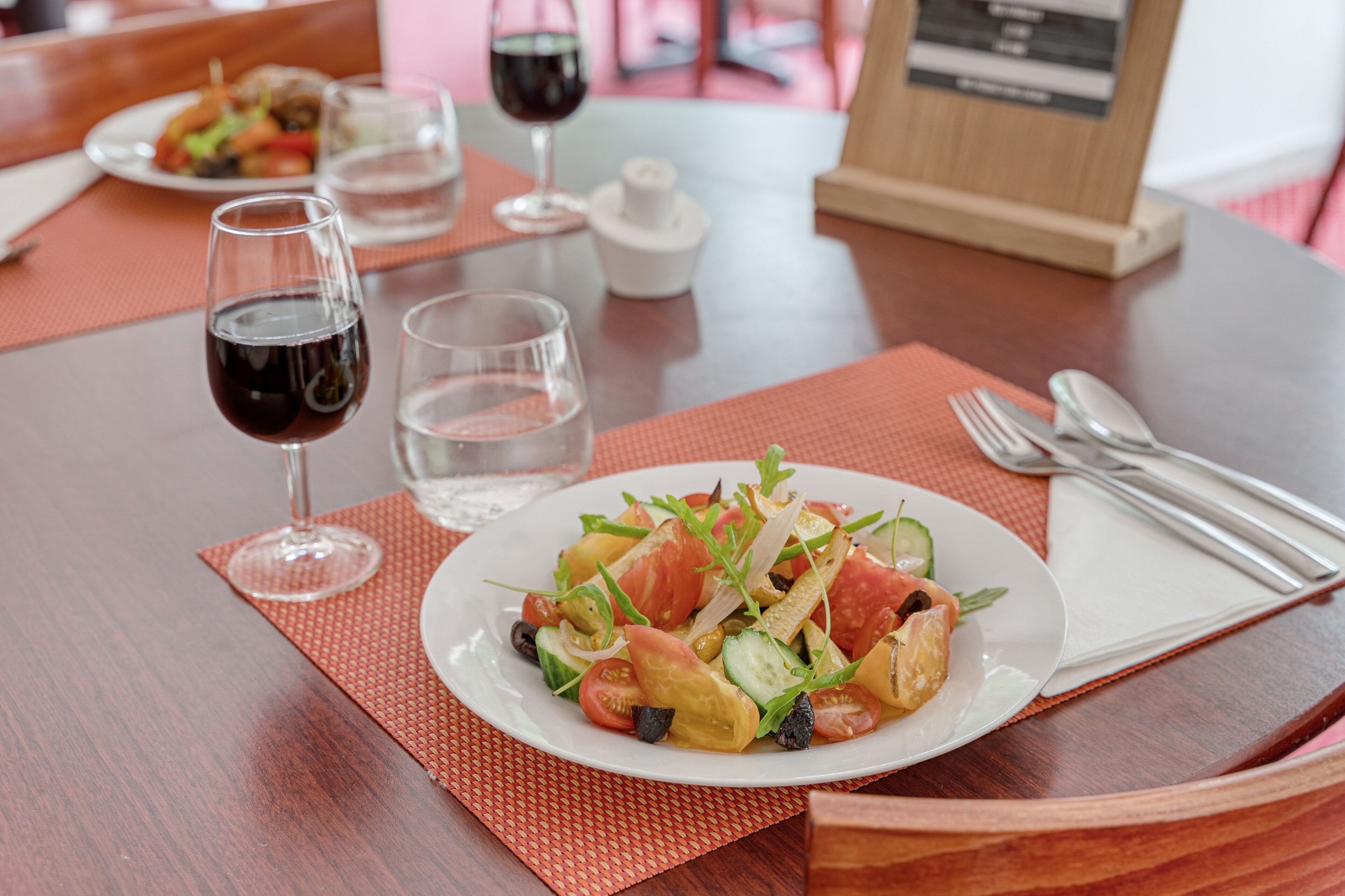 A dining table with a plate of salad, two wine glasses, and a water glass.
