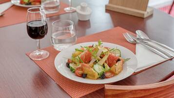A dining table with a plate of salad, two wine glasses, and a water glass.