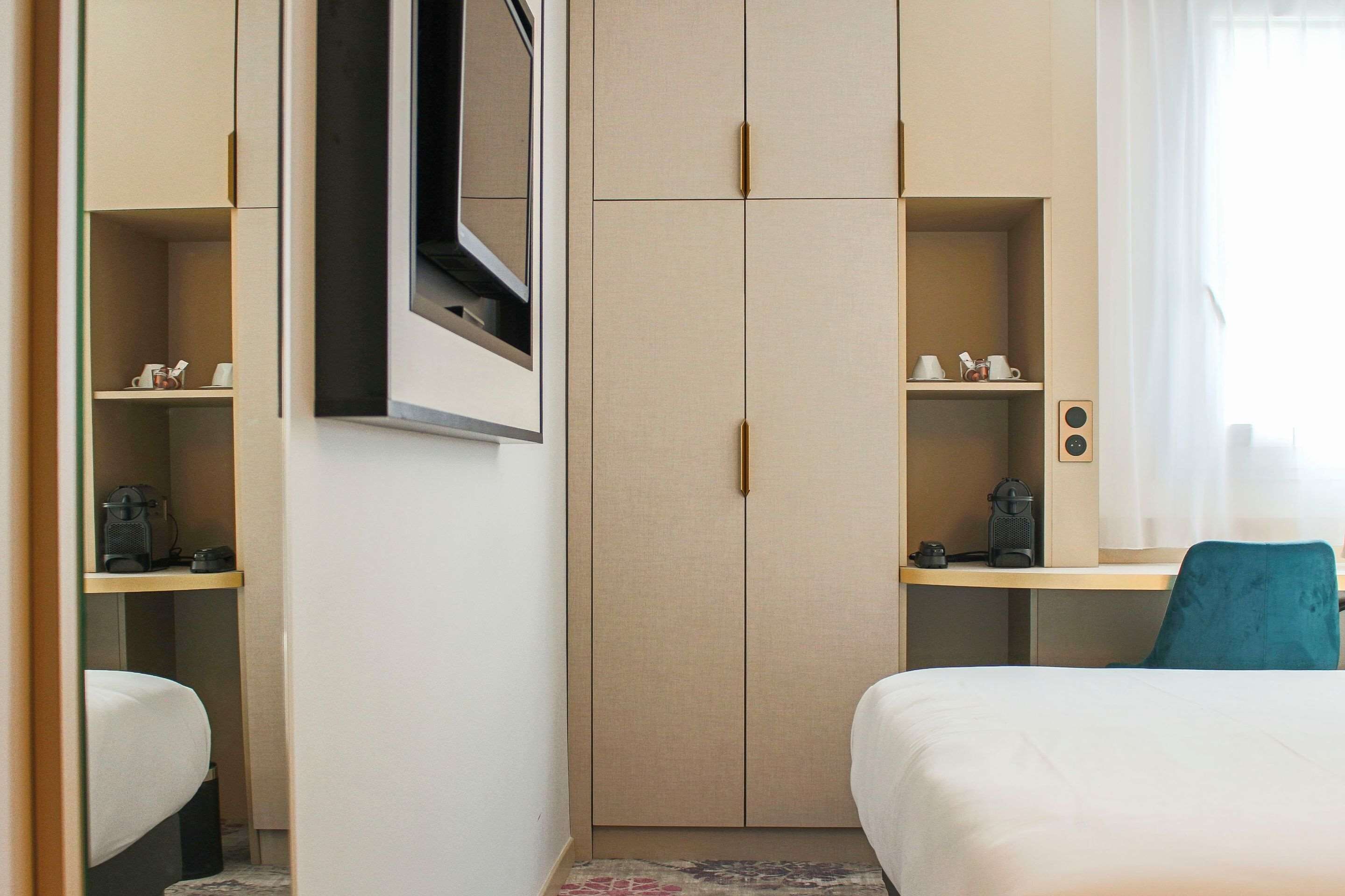 A hotel room with a bed, a desk, a wardrobe, and a television mounted on the wall.