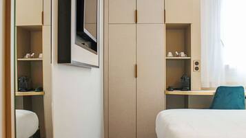 A hotel room with a bed, a desk, a wardrobe, and a television mounted on the wall.