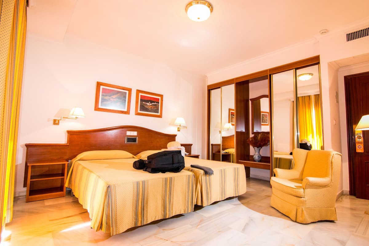 Ein Hotelzimmer mit einem Bett, einem Sessel, einem Nachttisch und einem Spiegel.