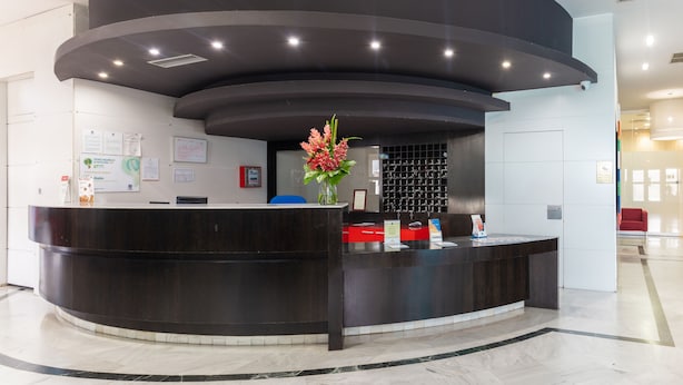 A modern reception desk with a curved design, a vase with flowers, and a blue chair. - Hotel Abades Loja (Loja)