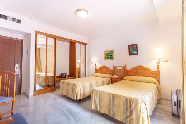 A hotel room with two beds, a wooden wardrobe, a chair, a bedside table, and a suitcase. - Hotel Abades Loja (Loja)